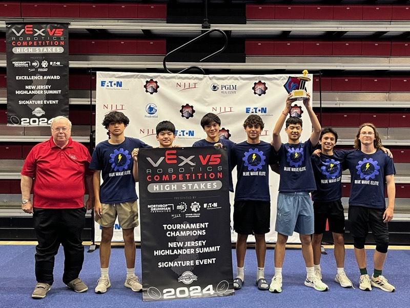 The team in matching shirts behind a Tournament Champions banner, one member holding the trophy overhead.