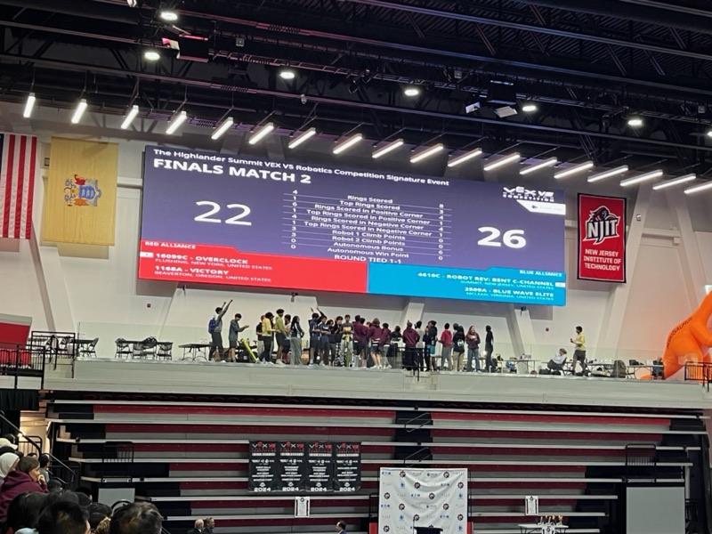 An arena scoreboard reading Finals Match 2, 26 to 22 with the round tied 1-1, Blue Wave Elite listed on the blue alliance.