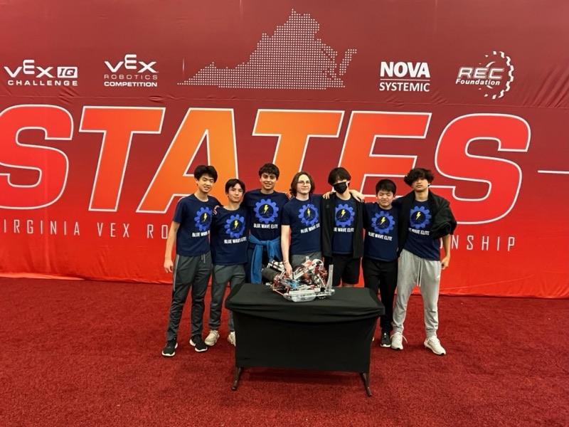 Seven team members in Blue Wave Elite shirts behind their robot on a table, in front of a giant STATES banner at the Virginia VEX Robotics Championship.