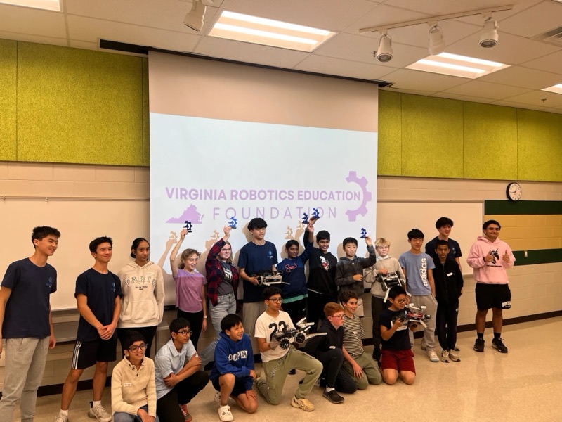 The whole workshop, mentors and builders together in front of the Virginia Robotics Education Foundation screen, trophies and robots held up.